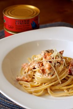 a white plate topped with pasta covered in sauce next to a can of canned tuna