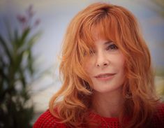 a woman with long red hair is looking at the camera while wearing a red sweater