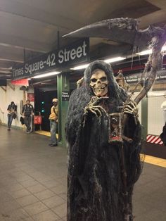 there is a man dressed up as a demon in the subway station with people walking by