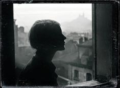 a black and white photo of a person looking out a window at the city below