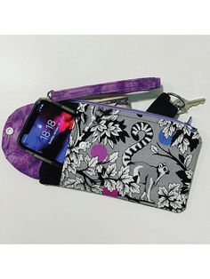 a cell phone in a purple and black floral print case with keychain attached to it