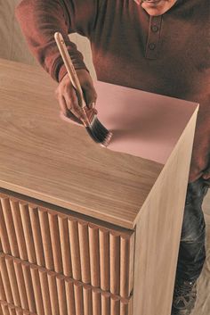 a man with a brush and paper on top of a wooden cabinet that is being used as a sideboard