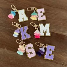 six charms with letters and tassels on them sitting on a table next to each other