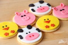 four decorated cookies with farm animals on top of each cookie, one is pink and the other is yellow