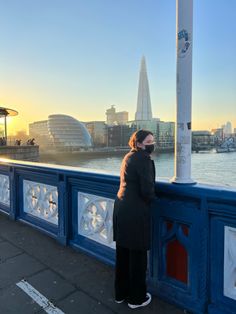 a woman standing on the side of a bridge looking at the water and buildings in the background