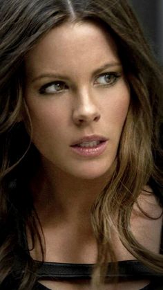 a woman with long brown hair and blue eyes looking at the camera while wearing a black dress