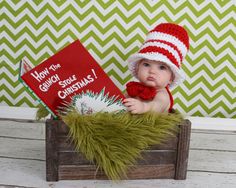 the baby is wearing a santa hat and holding a book while sitting in a crate