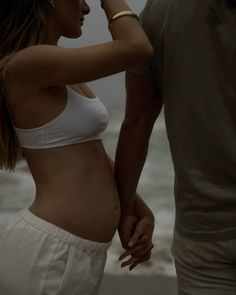 a man and woman standing next to each other near the ocean with their hands on their hips