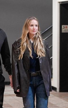 a woman walking down the street with a man in black jacket and jeans behind her