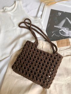 a brown crocheted bag sitting on top of a pair of white shorts next to a book