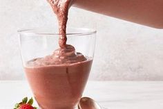 a person pouring chocolate into a glass with strawberries on the plate next to it