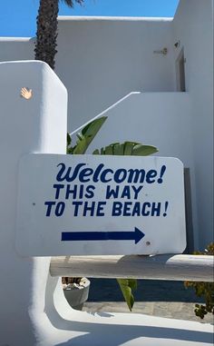 a welcome sign in front of a white building with palm trees and blue lettering on it