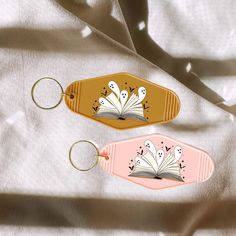 two book shaped keychains sitting next to each other on a white cloth covered surface