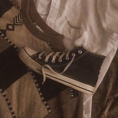 a pair of black converse shoes sitting on top of a bed next to a blanket