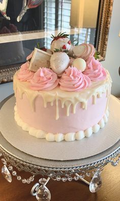 a pink and white frosted cake sitting on top of a table next to a mirror