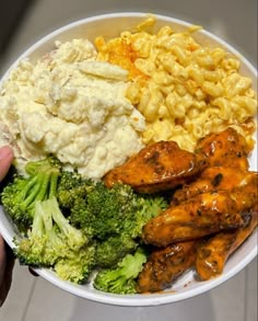 a person holding a plate with chicken, macaroni and broccoli