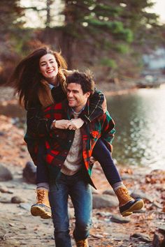 a man carrying a woman on his back while walking down a path by the water