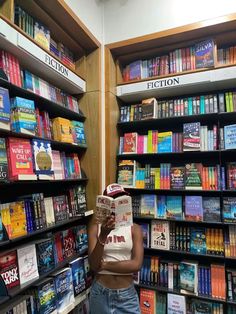 a woman standing in front of a bookshelf holding up a book to her face