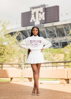 a woman is posing in front of the texas a & m stadium wearing a white dress and heels