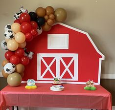 a red table topped with balloons next to a farm house and cowgirl's cake