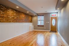 an empty room with hard wood flooring and brick wall in the background, there is a door leading to another room