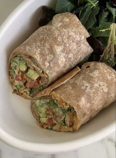 two burritos sitting on top of a white plate next to a green salad