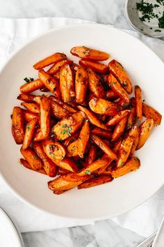 a white bowl filled with cooked carrots on top of a marble table next to silverware