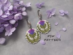 two small beaded earrings sitting next to purple flowers on a gray surface with the words pattern written below them