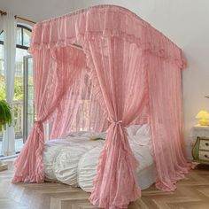 a pink canopy bed sitting in a bedroom next to a window