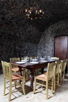 a dining room table with six chairs and a wine glass set on it in front of a stone wall