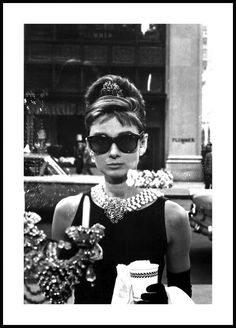 a woman in black dress and sunglasses standing next to a table with jewelry on it