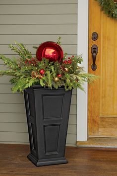 a black planter filled with greenery and christmas decorations on the front porch next to a door