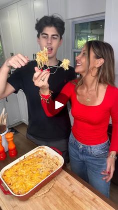 a man and woman standing in front of a dish of macaroni and cheese