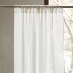 a white curtain hanging on the side of a window sill in front of a tree