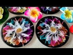 four plates with colorful flowers on them sitting on a counter top in front of candles