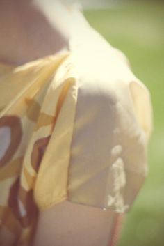 a woman wearing a yellow dress with circles on it's chest and back, standing in the grass