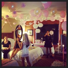 three women standing in front of a bed with pink and white balloons