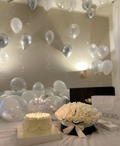 a table topped with two cakes covered in white frosted icing next to balloons