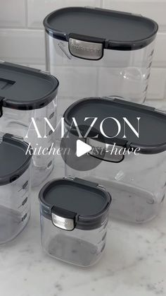 four clear storage containers with lids on a marble countertop in front of a white tile backsplash