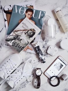 the contents of a woman's purse laid out on a marble counter top with magazine, watch and other items