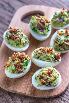 deviled eggs filled with guacamole and bacon on a wooden platter