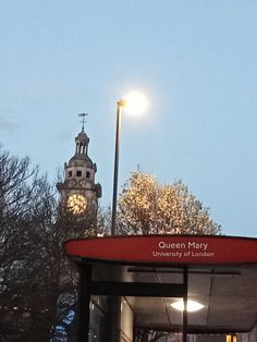 a bus stop with a clock tower in the back ground and trees on either side