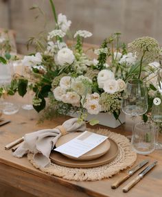 a wooden table topped with lots of white flowers and greenery on top of it