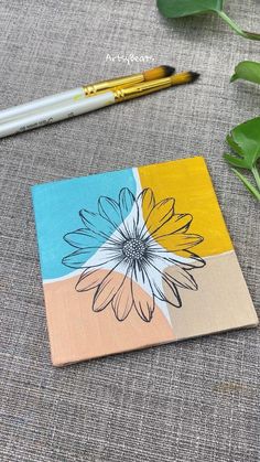 a flower painted on a piece of paper next to a pen and plant with leaves