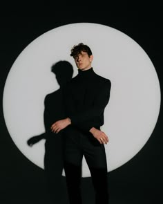 a man standing in front of a white circle with his shadow on the wall behind him