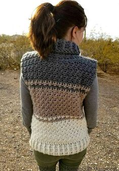 a woman standing in the dirt with her back to the camera, wearing a gray and white crocheted sweater