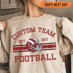 a woman wearing a sweatshirt with the words custom team est football printed on it and an image of a football helmet