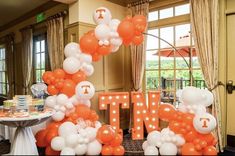 an orange and white balloon arch with the letter t on it in front of a table