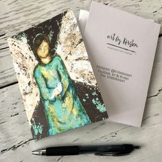 a notepad with an angel painting on it next to a pen