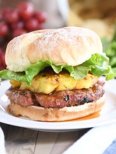 a hamburger with lettuce and pineapple on it sitting on a white plate